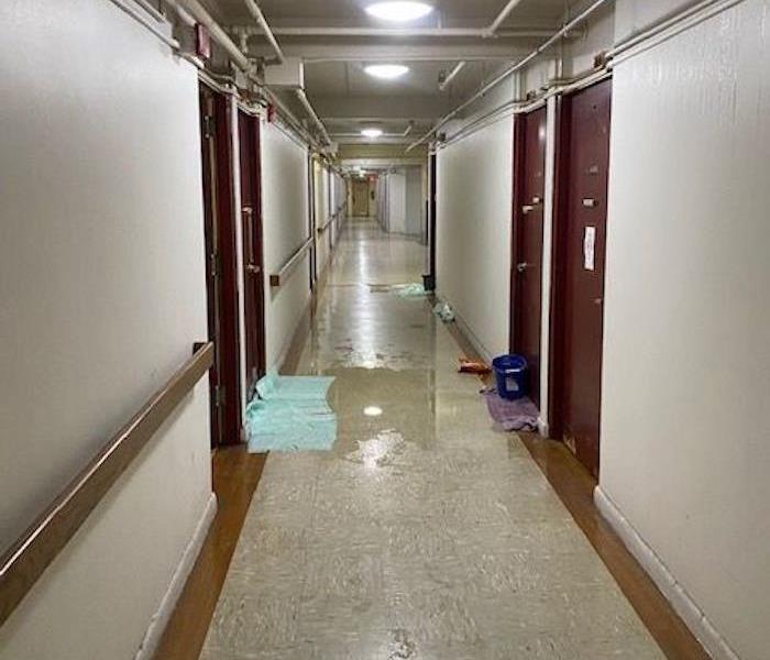 Flood-damaged apartment hallway with standing water and towels outside of doorways