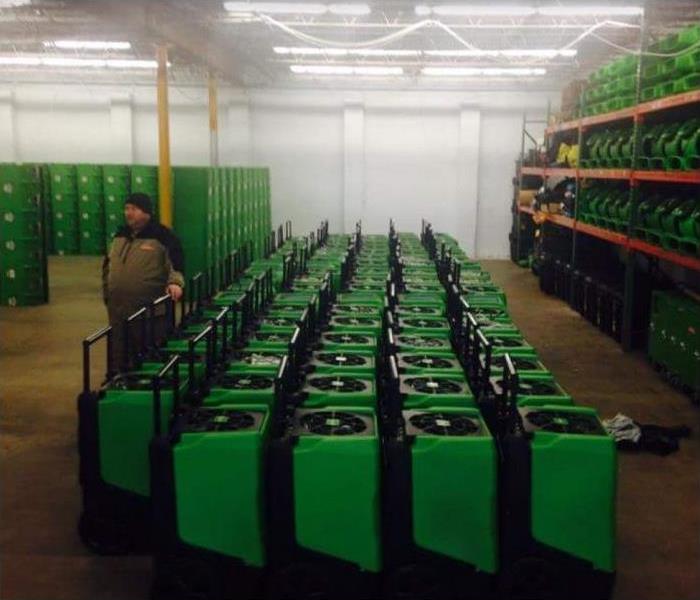 SERVPRO storage facility with restoration equipment stacked; SERVPRO tech standing in warehouse